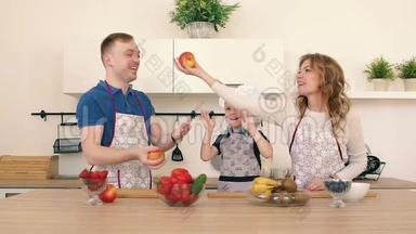 一家人正在<strong>厨房</strong>准备沙拉.. <strong>爸爸</strong>和妈妈把苹果扔起来。 儿子在笑。